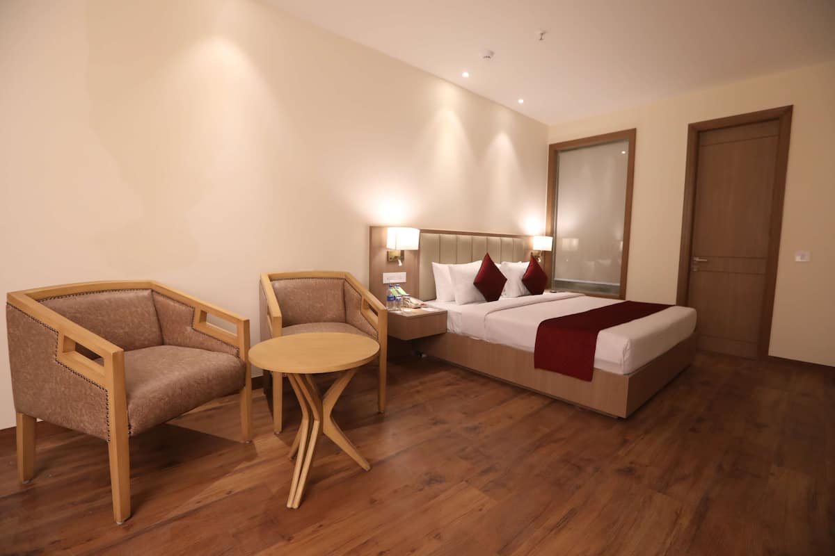Una habitación de hotel con una cama, dos sillones, una mesita redonda, una mesita de noche y un espejo.