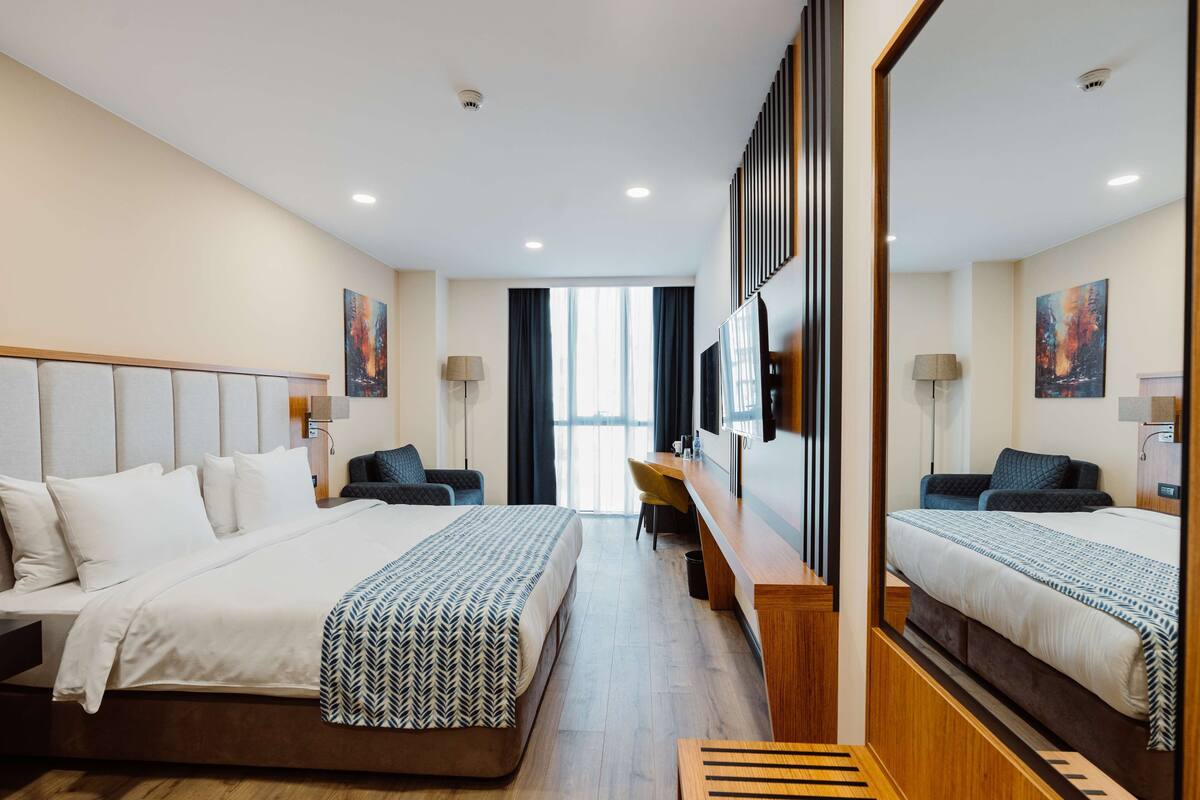 A hotel room with a large bed, a desk, a chair, and a TV.