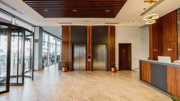 A modern lobby with a marble floor, wooden reception desk, elevators, and large windows.