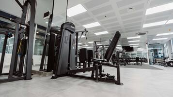 Un gimnasio con diversas máquinas de ejercicio, un muro espejado y suelo de baldosas.