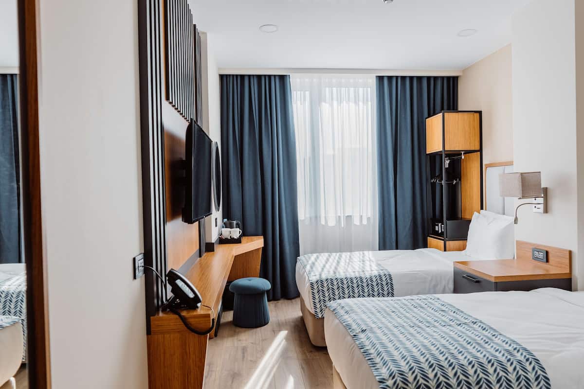 A hotel room with two beds, a desk, a TV, a lamp, and a window with curtains.
