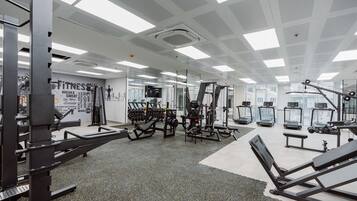 Een sportschool met diverse fitnessapparaten, spiegelwanden en een plafond met vierkante lampen.
