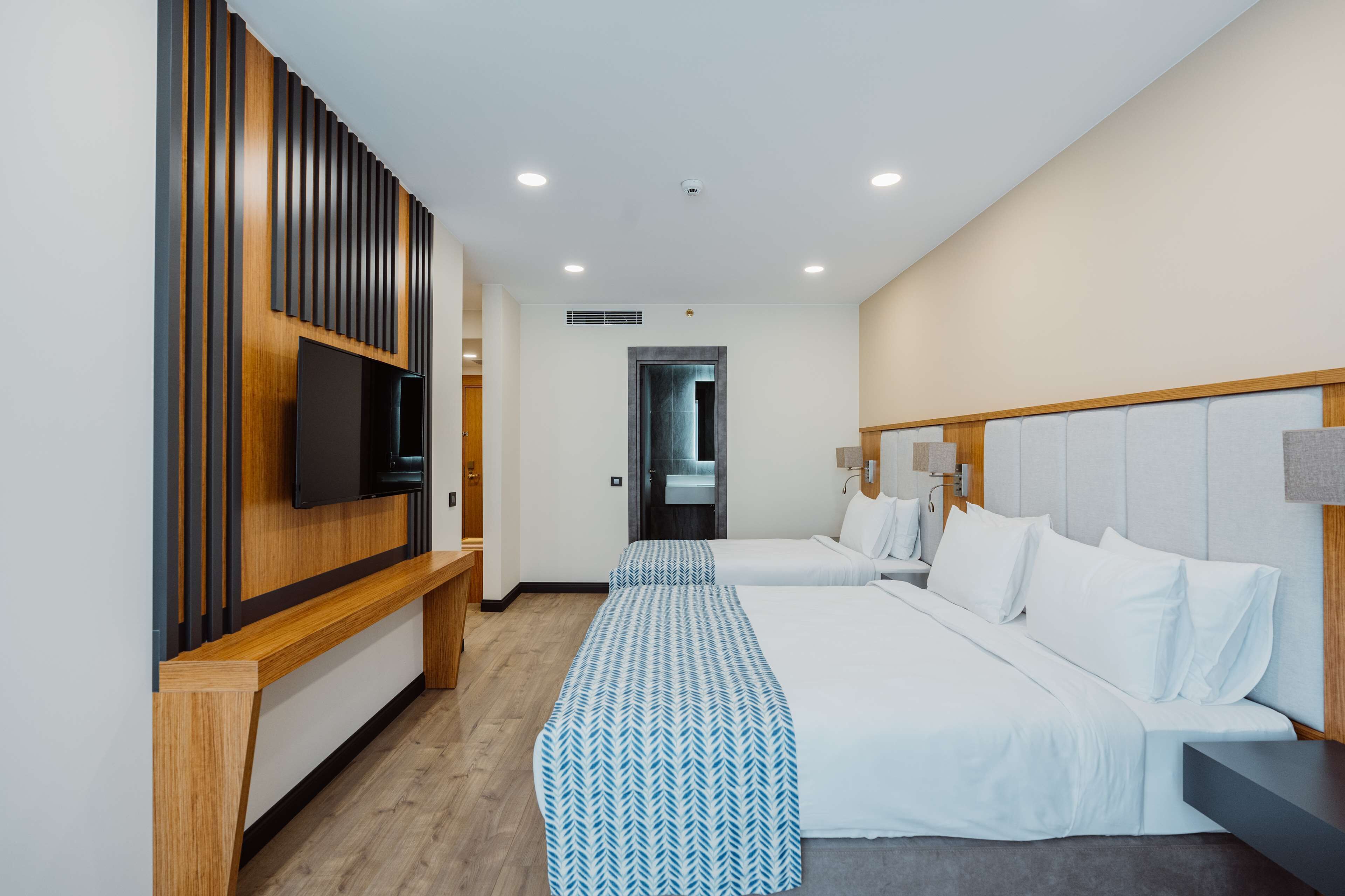 Una habitación de hotel moderna con dos camas, un televisor, un panel de pared de madera y un banco.