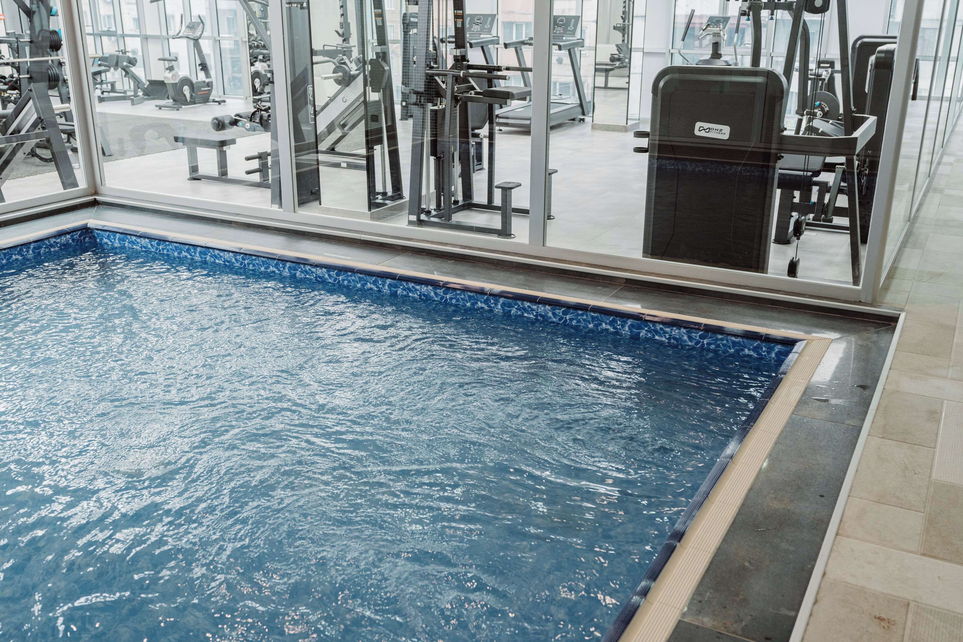 Een binnenzwembad met fitnessapparatuur op de achtergrond.