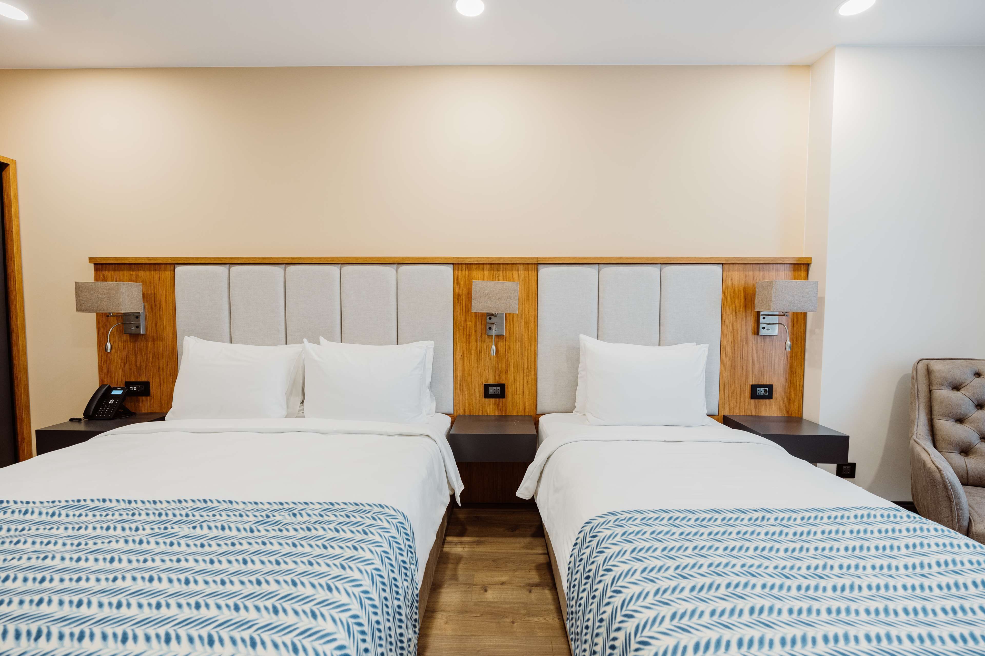 Camera d'albergo con due letti, testiere in legno, lampade sui comodini, telefono e una sedia.
