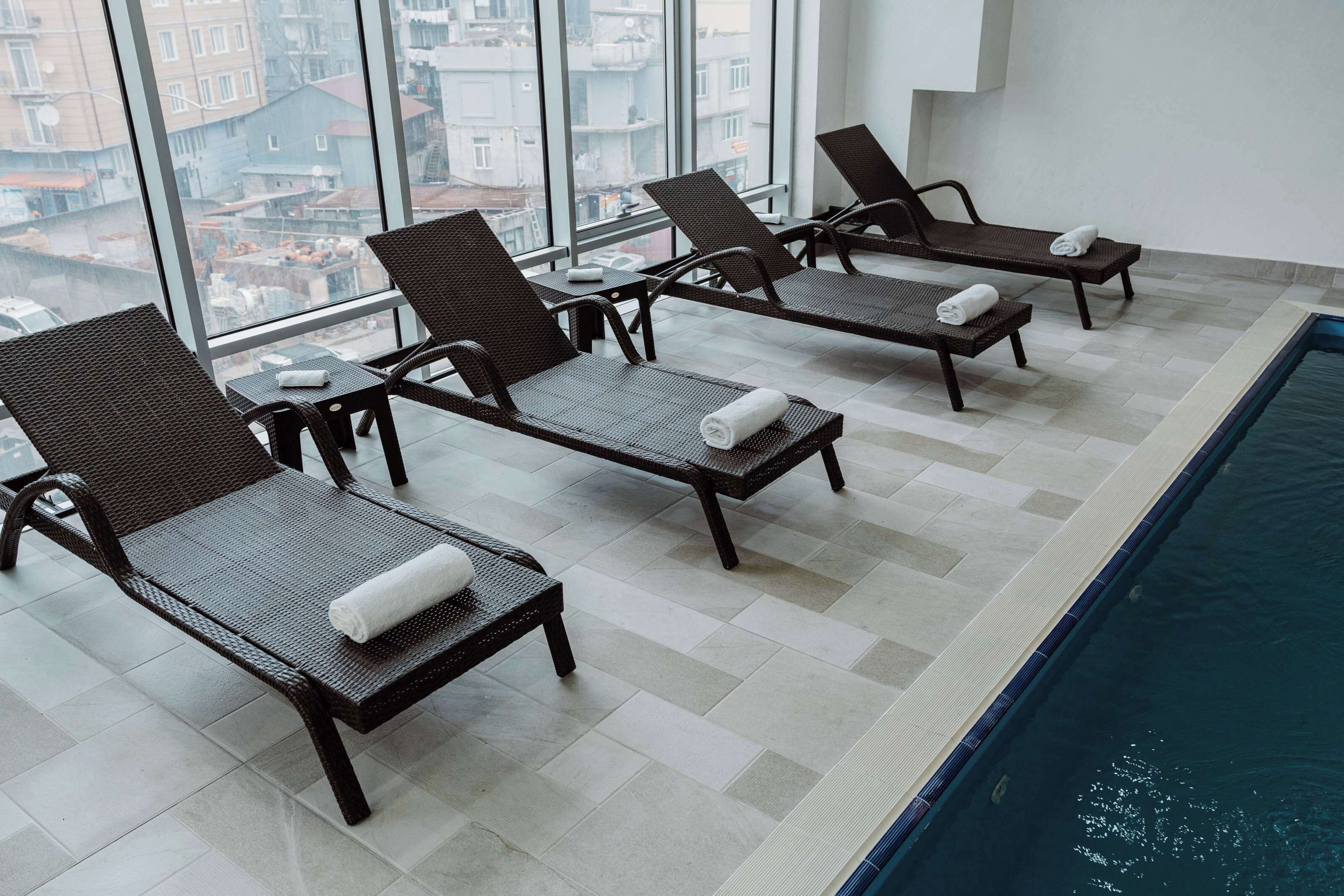 Zona de piscina con sillones de descanso y vistas a la ciudad a través de amplias ventanas.