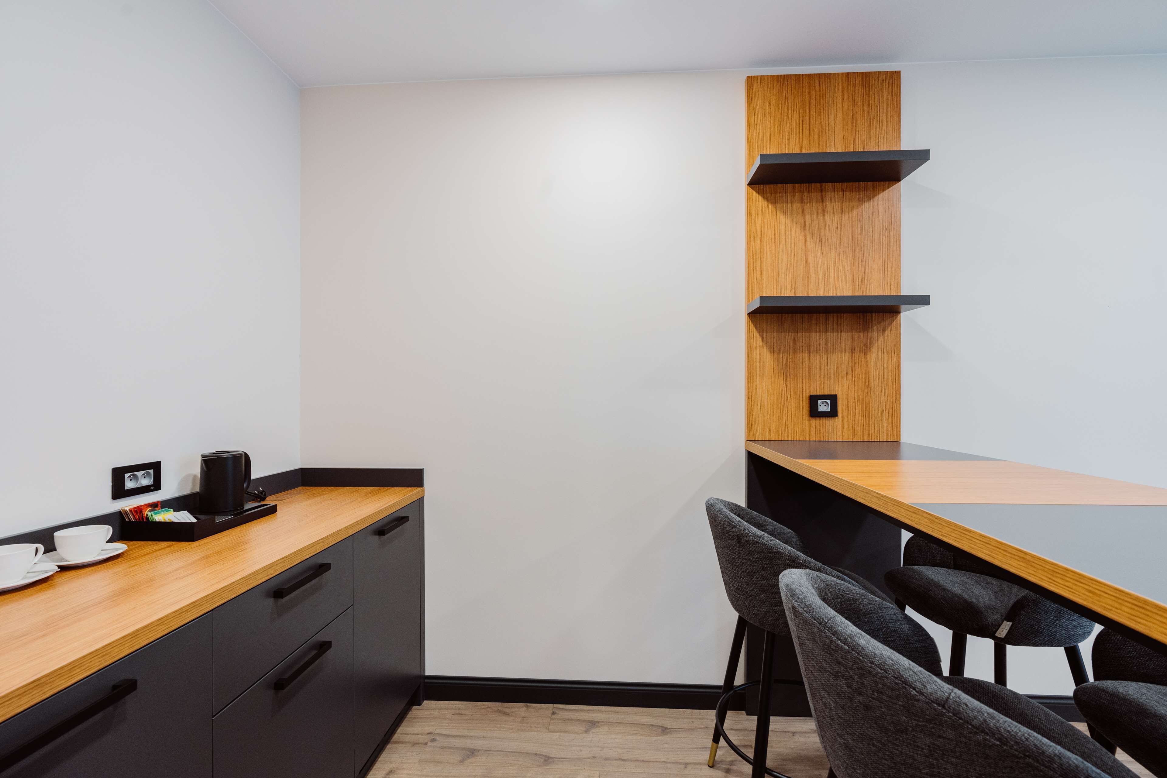 Una cocina moderna con encimera de madera, armarios negros y una unidad estante de madera empotrada.