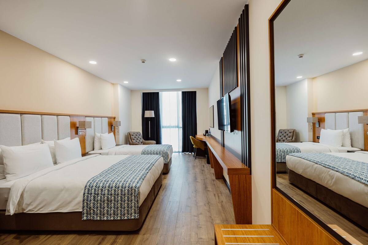 A hotel room with two beds, a desk, a mirror, and a TV.