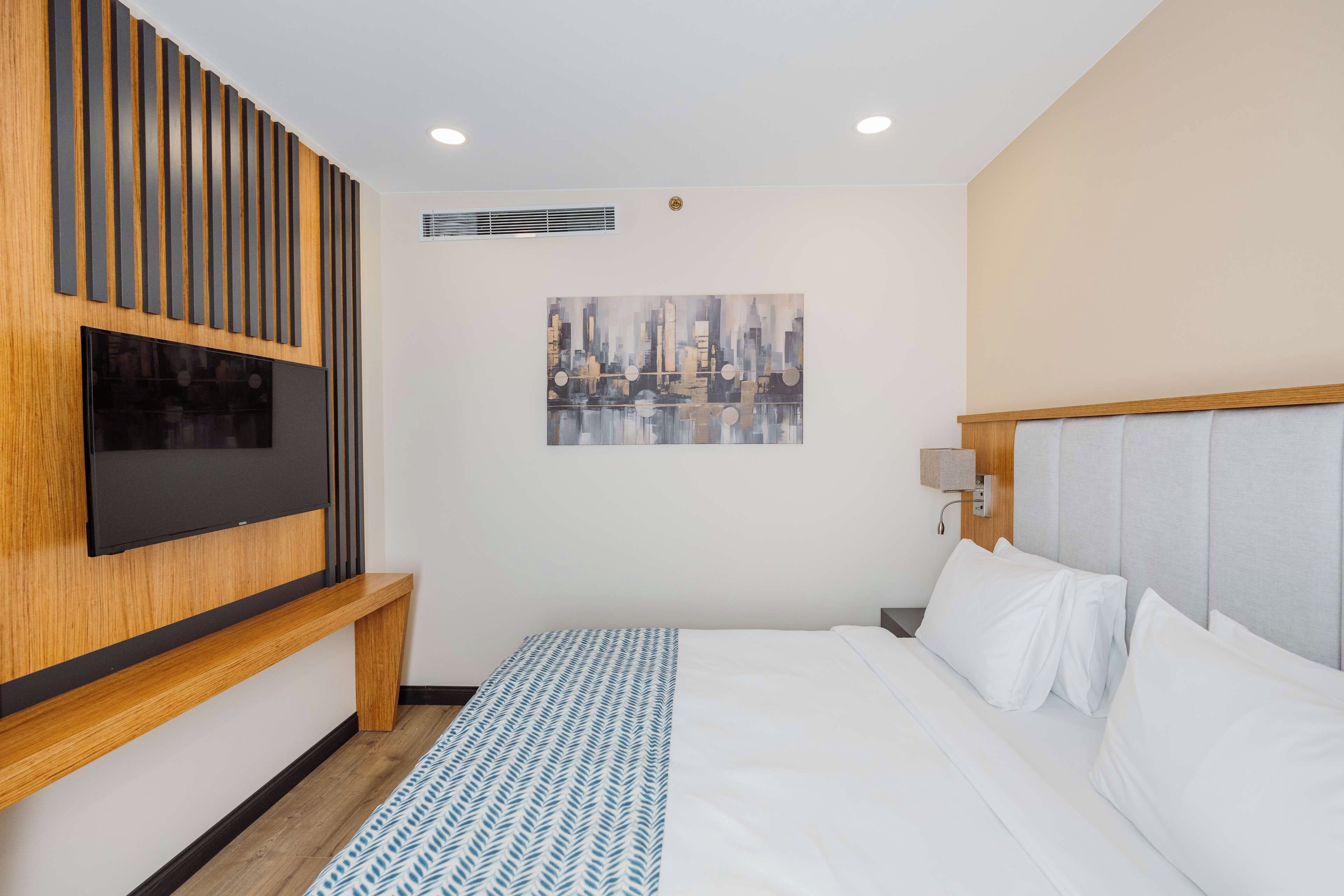 Ein Hotelzimmer mit einem Bett, einem an der Wand montierten Fernseher, einem Gemälde und einer Bank.