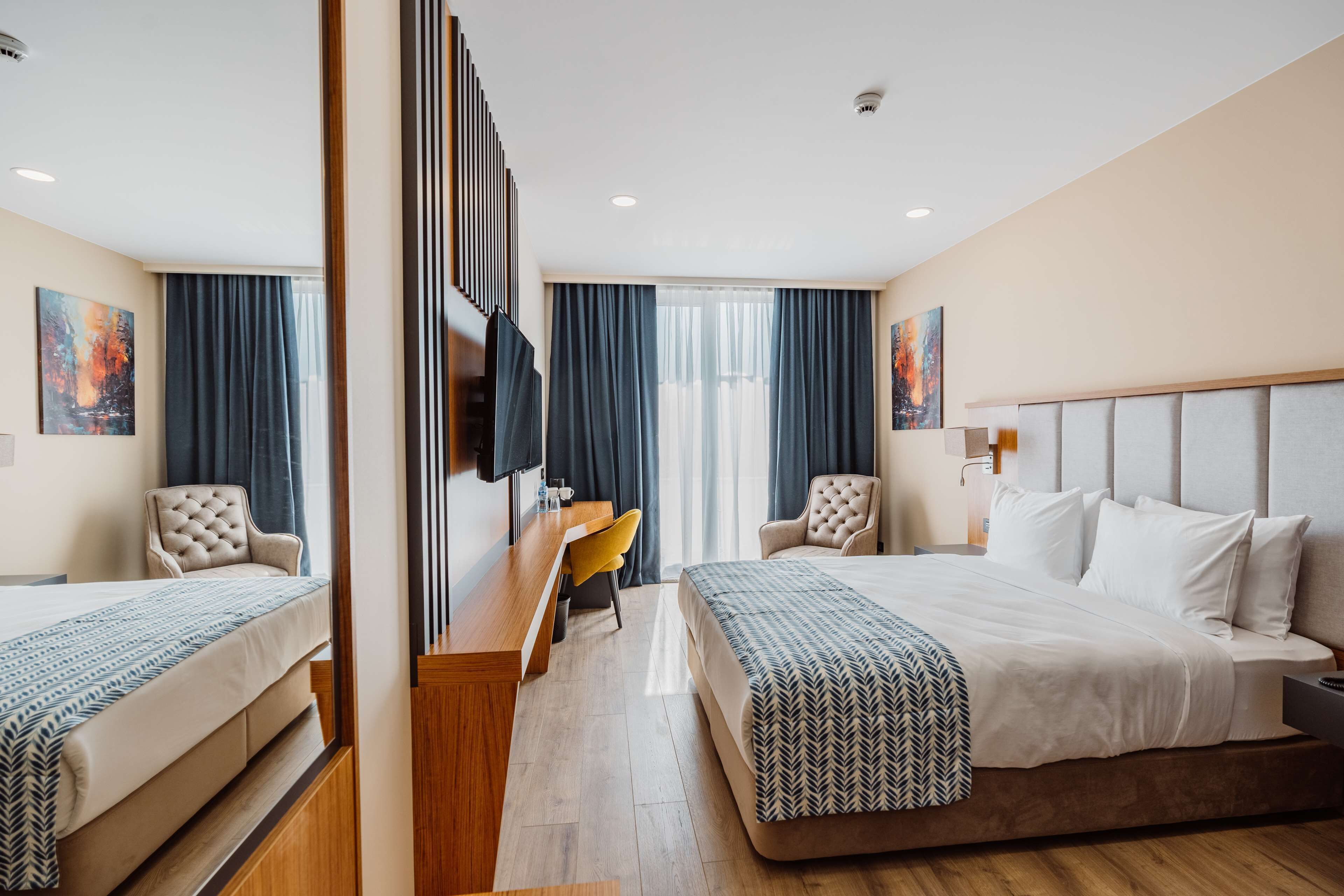 Una habitación de hotel con una cama grande, un escritorio con silla, televisión y una ventana con cortinas.