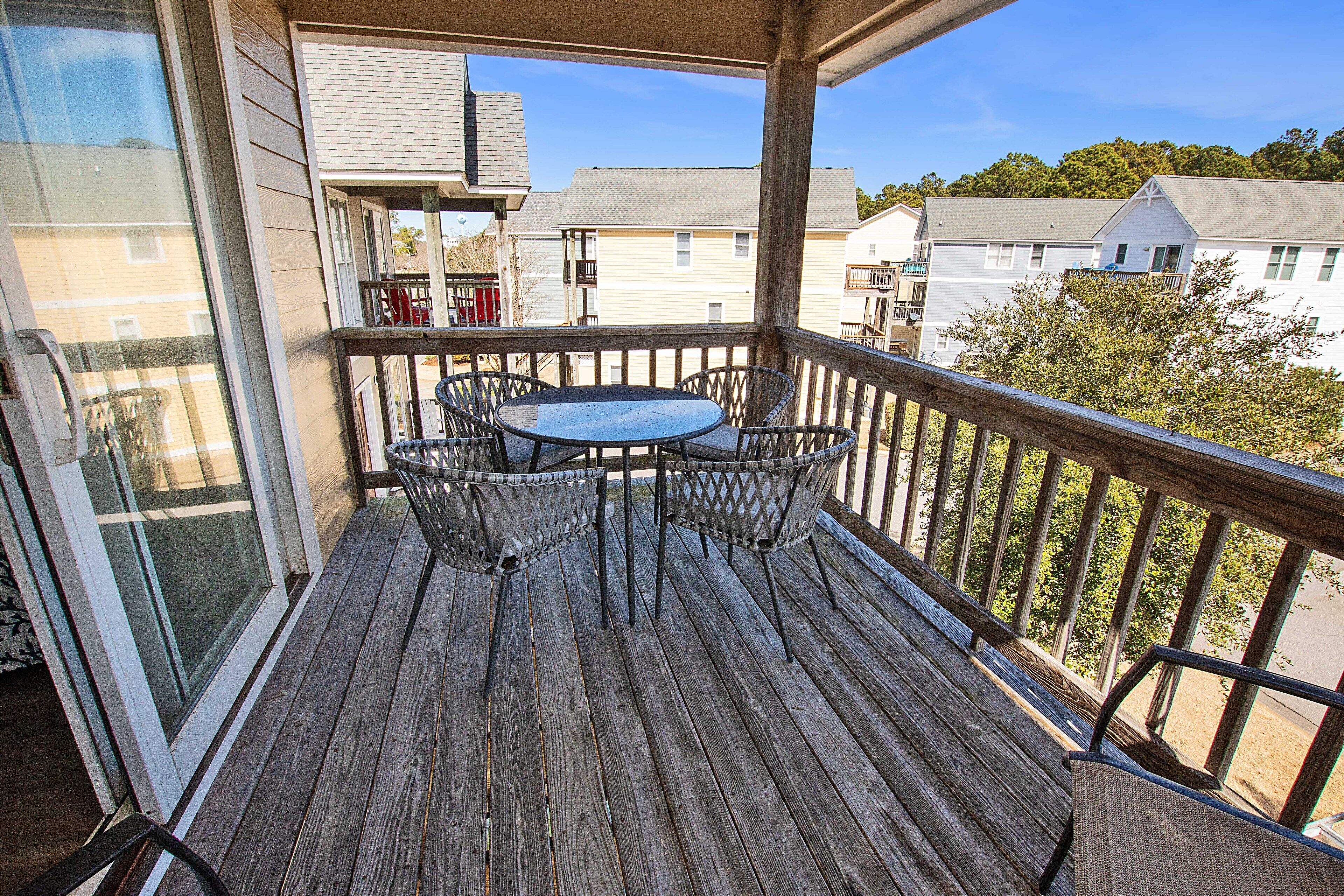 Une terrasse en bois avec une table ronde et quatre chaises, donnant sur un quartier résidentiel.