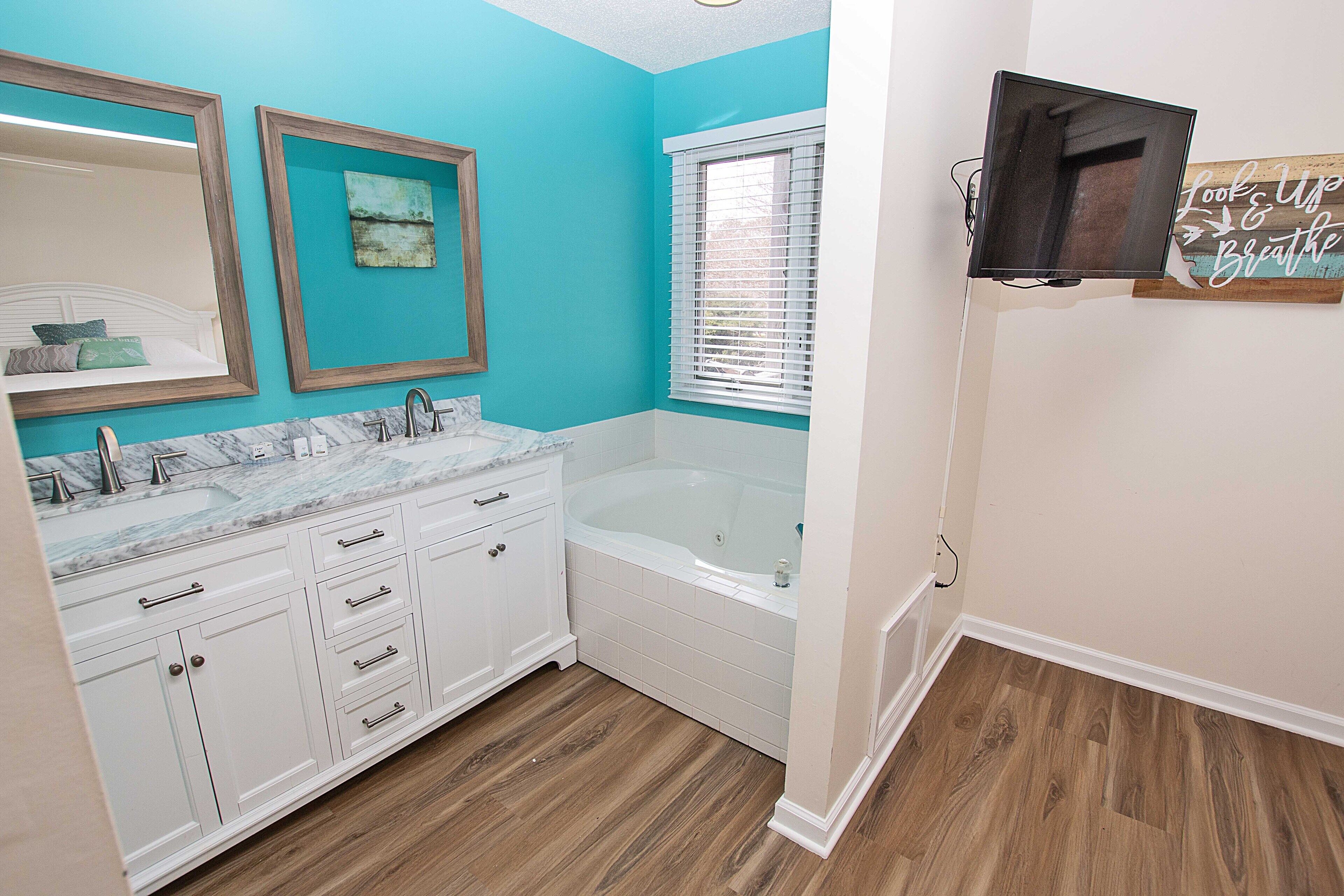 A bathroom with a large mirror, two sinks, a bathtub, and a window with blinds.