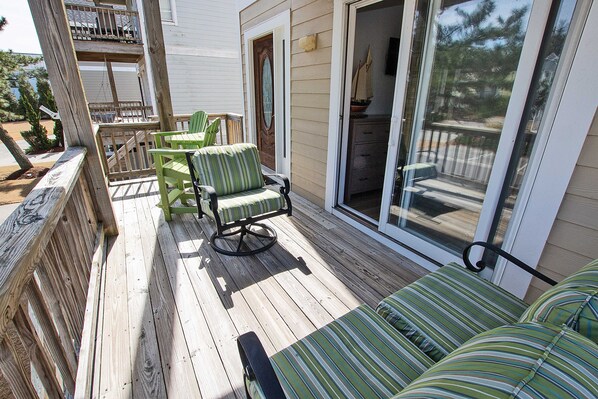 A wooden deck with a green-striped sofa and chairs, a sliding glass door, and a small table.
