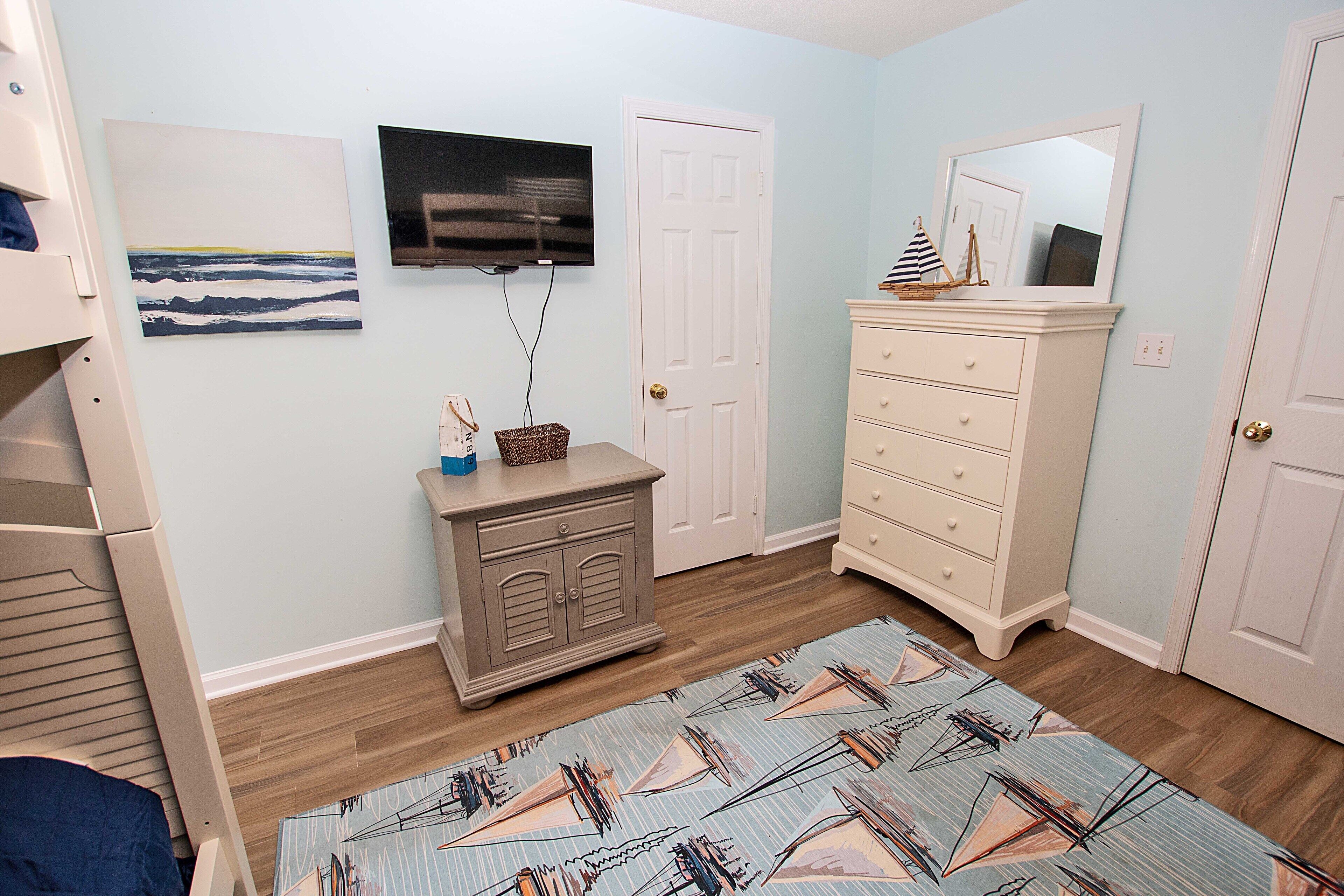 A bedroom with a bed, dresser, television, and artwork on the wall.