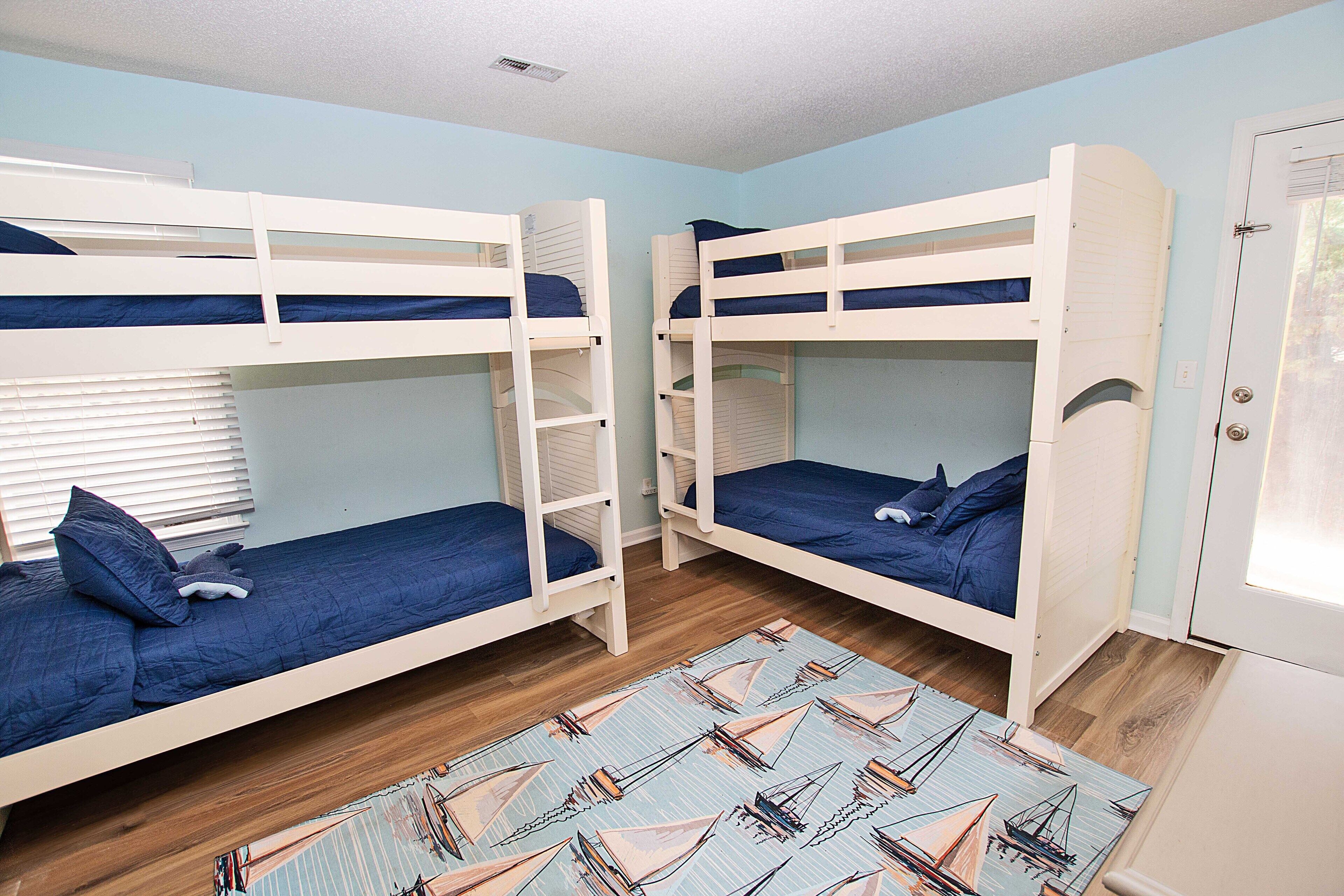 A room with bunk beds, a wooden floor, and a patterned rug.