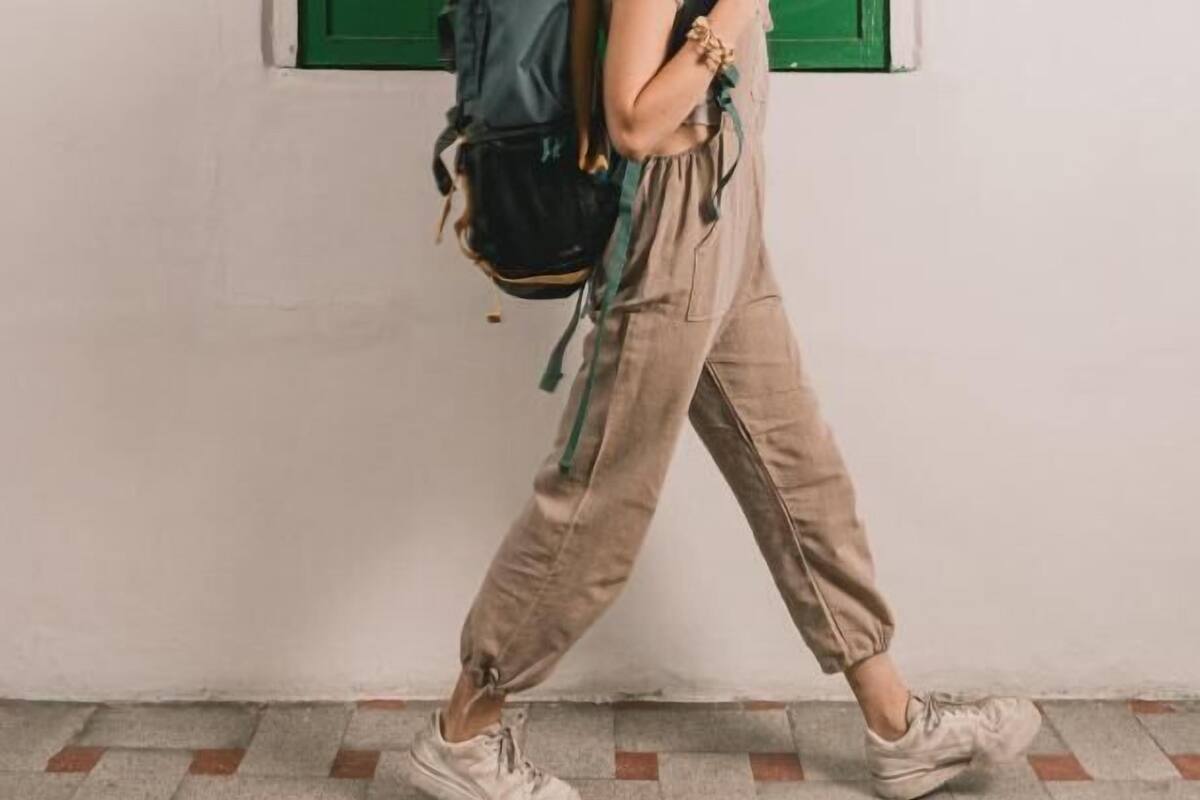A person walking indoors with a backpack, a window with green shutters, and a tiled floor.