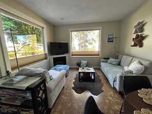 A living room with a sofa, a coffee table, a TV, and a bookshelf. - Welcome Kye Bay Nest at  the beach - relax, restore, and explore. H820823952 (Comox)