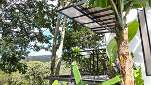 A covered outdoor seating area with a metal railing, surrounded by lush greenery and trees.