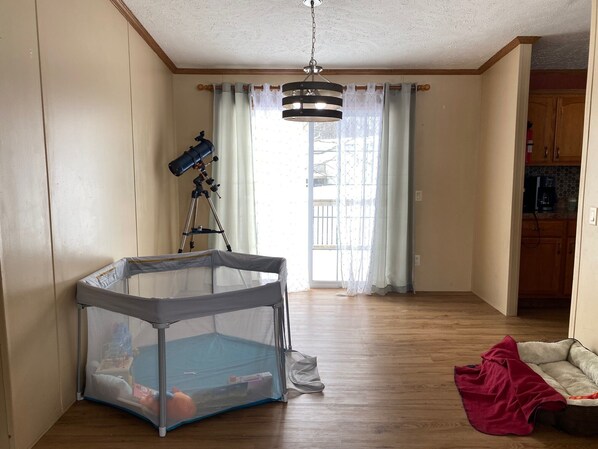 A room with a wooden floor, a telescope, a playpen, and a pet bed.