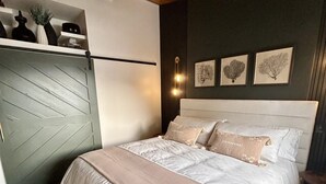 A bedroom with a bed, a wooden ceiling fan, a wall-mounted shelf with decorative items, and framed artwork. - Birch Bayside Retreat - AC, Pet Friendly & Close to the Beach! Luxury 2 Bedroom (Blaine)
