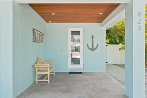 A covered porch with a wooden ceiling, a door with an anchor decoration, a wooden bench, and a number '423' on the wall. - Jersey Girl by Duncan Real Estate (Anna Maria)