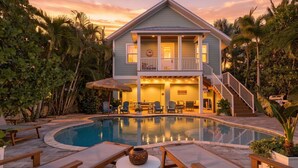 Ein zweistöckiges Haus mit Pool, Sitzgelegenheiten im Freien und einer Treppe, die zu einem Balkon führt.