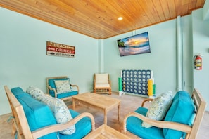A room with a wooden ceiling, a television mounted on the wall, a sign indicating beach, drinks, and fishing, and a fire extinguisher. - Jersey Girl by Duncan Real Estate (Anna Maria)