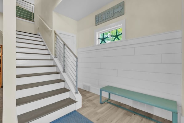 A staircase with a metal railing, a bench, a window with a star decoration, and a wall sign that reads 'BEACH'. - Jersey Girl by Duncan Real Estate (Anna Maria)