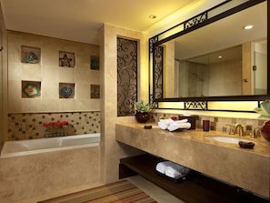 Un baño con bañera, dos lavamanos, un espejo grande, azulejos decorativos y un estante pequeño con toallas.
