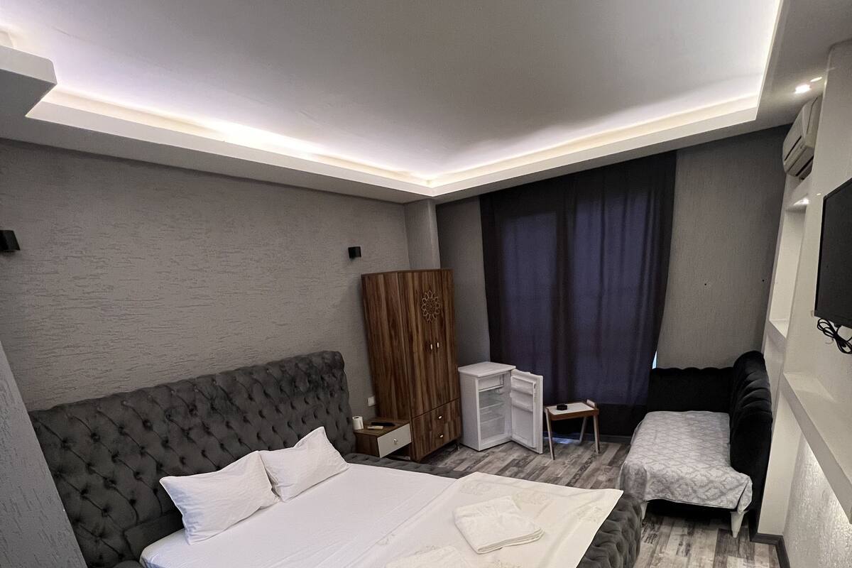 A modern hotel room with a large bed, a wardrobe, a desk, and a TV.