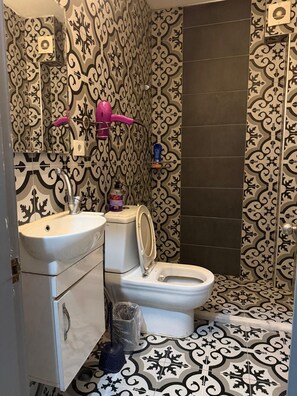 A bathroom with a patterned wallpaper, a white sink, a toilet, and a shower area. - Aden otel (Bursa)