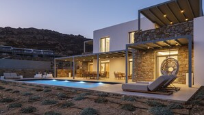 A modern house with a swimming pool, outdoor seating, and a stone wall.