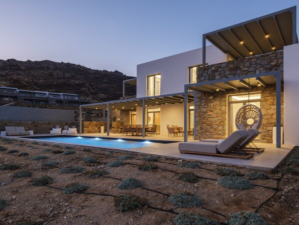 A modern house with a swimming pool, outdoor seating, and a stone wall.