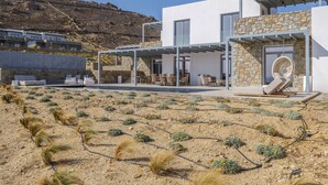 A modern house with a stone exterior, a covered patio with outdoor furniture, and a view of a dry, rocky landscape.