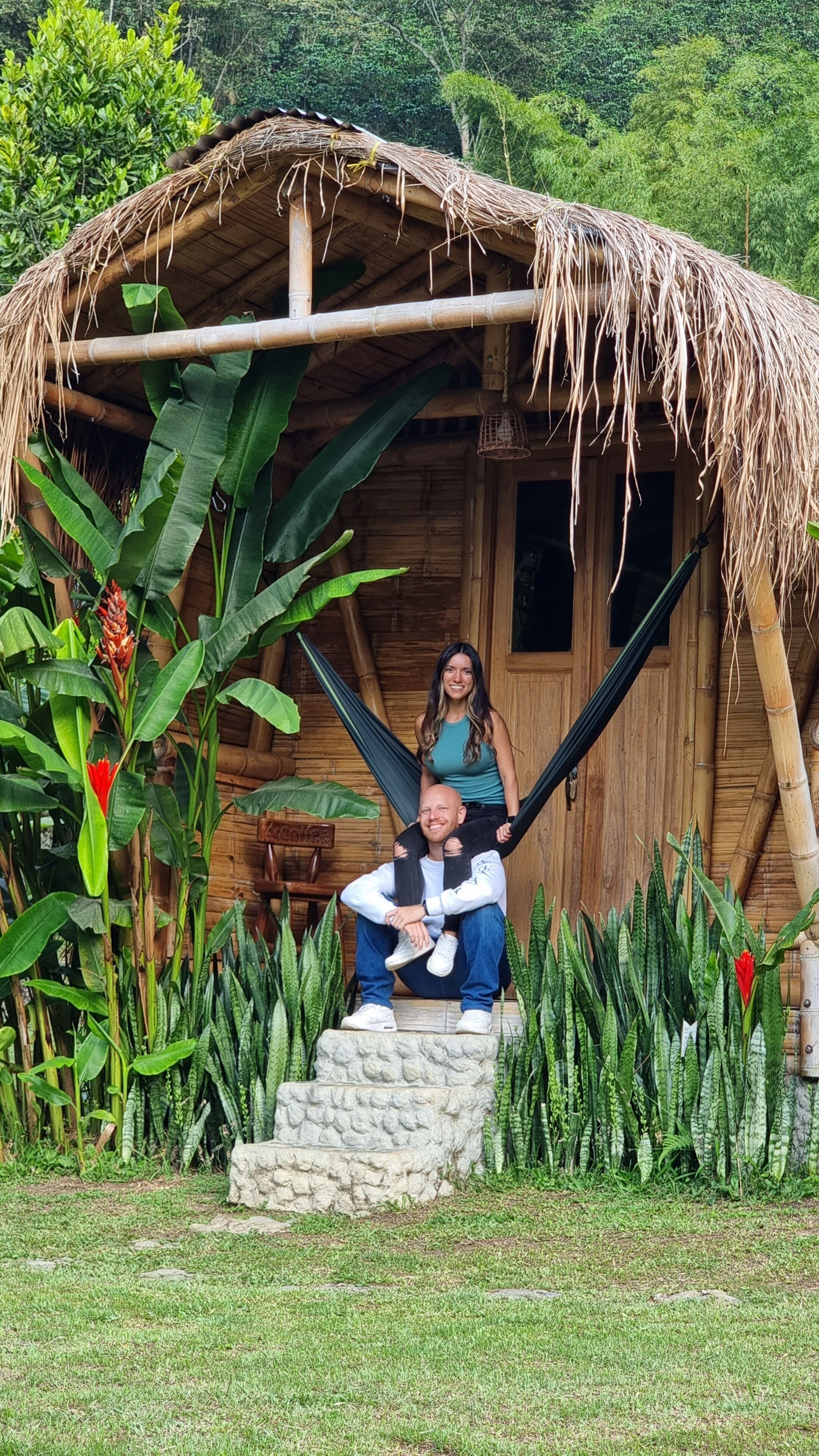 A rustic wooden hut with a thatched roof, surrounded by lush greenery and tropical plants.