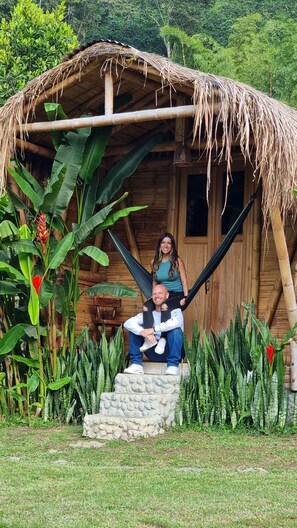 A rustic wooden hut with a thatched roof, surrounded by lush greenery and tropical plants.