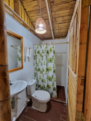 A bathroom with a wooden ceiling, a white sink, a toilet, and a shower curtain with a leaf pattern.