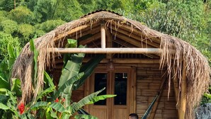 A wooden hut with a thatched roof, surrounded by lush greenery and banana plants. - Pradera Ecoliving (Betania)