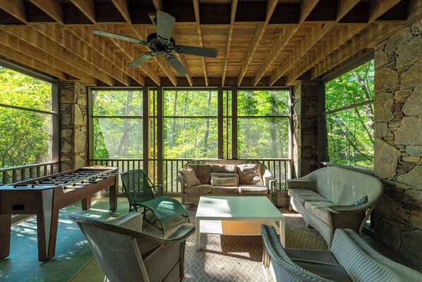A covered outdoor area with a foosball table, seating, and a ceiling fan.