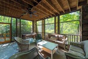 Un espacio exterior cubierto con mesa de fútbol de mesa, mobiliario de mimbre y ventanas amplias con vista al bosque.
