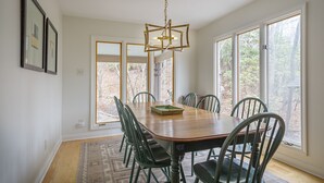 A dining area with a wooden table, six chairs, a chandelier, and large windows. - Heavenfell | Spacious Montreat Home | 1 Mile from Lake Susan & Conference Center! (Montreat)