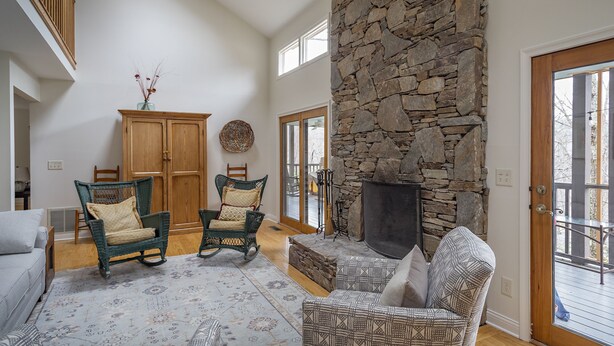 A spacious living room with a stone fireplace, two wicker chairs, a patterned rug, and a wooden cabinet. - Heavenfell | Spacious Montreat Home | 1 Mile from Lake Susan & Conference Center! (Montreat)