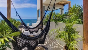 Un hamac suspendu sous une pergola en bois, d’où l’on aperçoit une piscine et une vue sur l’océan.