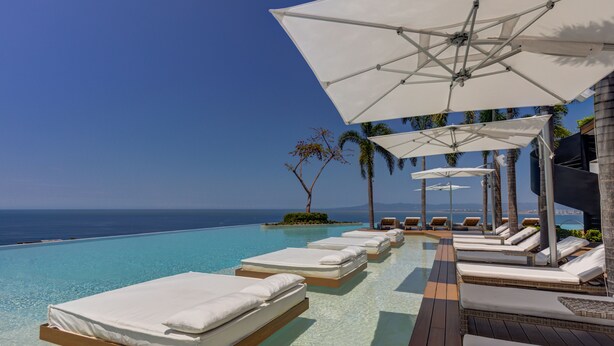 Area piscina con lettini e ombrelloni, vista su un oceano blu cristallino.