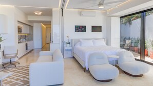 Una camera d'hotel moderna con un letto, due poltrone bianche, un tavolino e una ventola a soffitto.