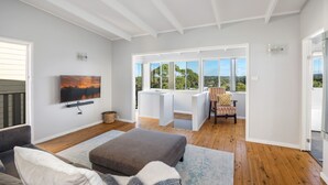 Ein geräumiges Wohnzimmer mit großem Fernseher, bequemen Sitzgelegenheiten, einem Balkon mit Aussicht und ansprechendem modernen Design.