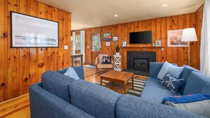 A living room with a sofa, coffee table, fireplace, TV, and wooden walls.