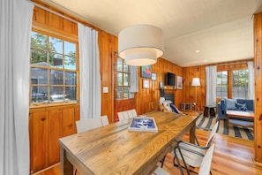 A wooden-paneled room with a dining table, chairs, a sofa, and a television.