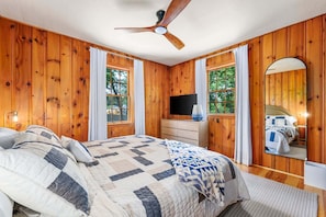 Camera da letto con pannelli in legno, un letto, una televisione, una ventola a soffitto e un grande specchio.