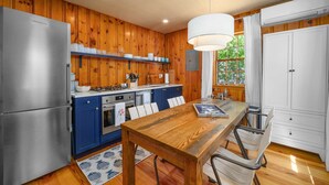 A kitchen with wooden walls, a stainless steel refrigerator, a stove, and a dining table with chairs.